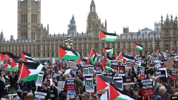 Protesters hold placards and wave Palestinian flags as they walk over Westminster Bridge with the Palace of Westminster, home of the Houses of Parliament behind during a 'March For Palestine' in Lo<em></em>ndon on October 28, 2023, to call for a ceasefire in the c
