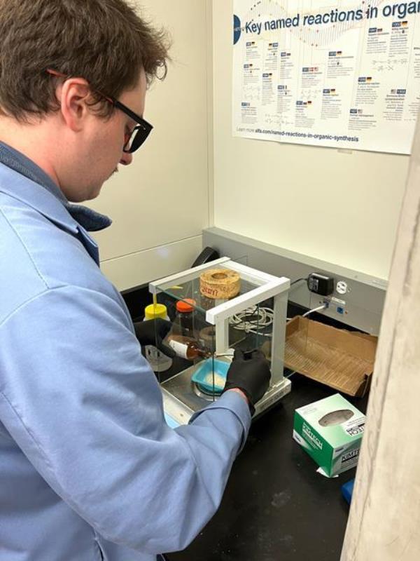 A scientist in a lab measuring out some crystals o<em></em>nto some scales