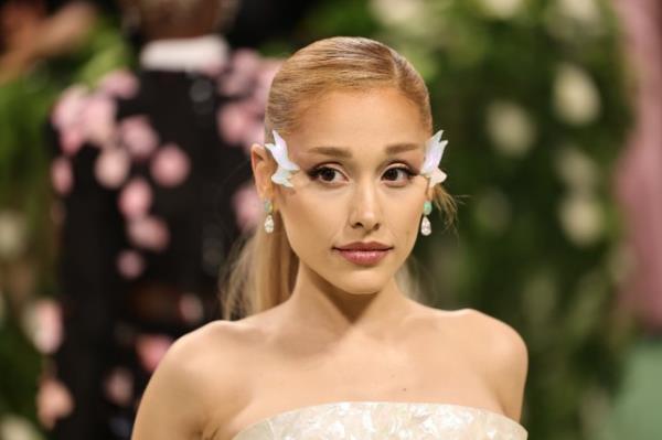 Ariana Grande wearing a white dress and wing embellishments on her face