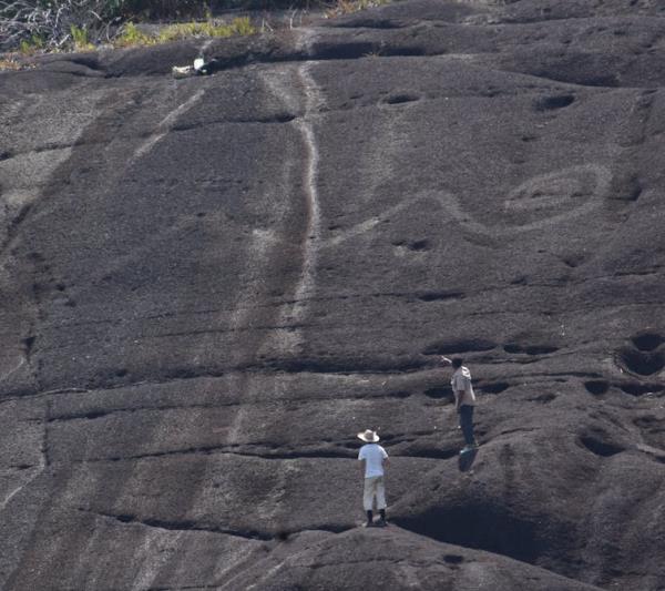 Telephoto shot of mo<em></em>numental rock art of snake tail in Colombia, humans for scale.
