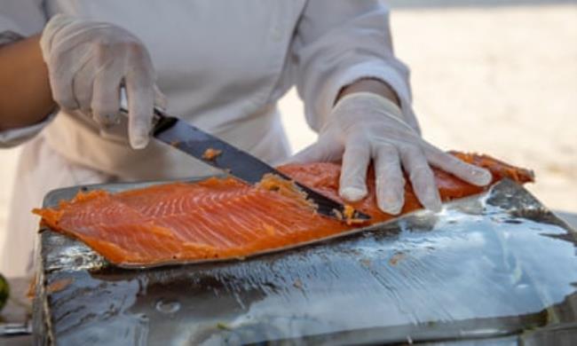 A chef cuts slices of salmon from a large fillet 