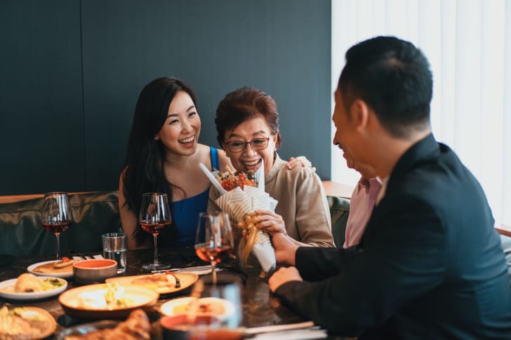 a man and woman ho<em></em>noring a mother with flowers at a restaurant
