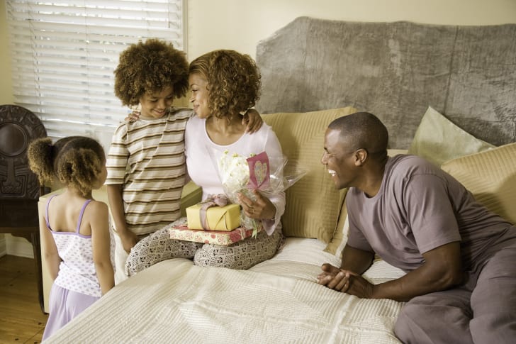 dad and two children giving a mom mother's day gifts in bed