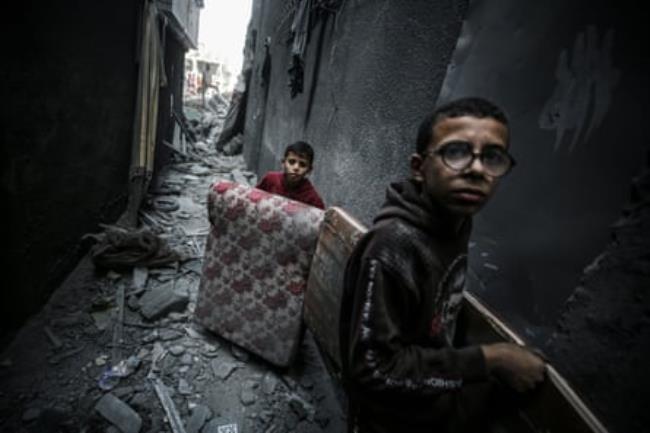 Palestinian children carry a mattress and a table through the alleyways of Gaza.
