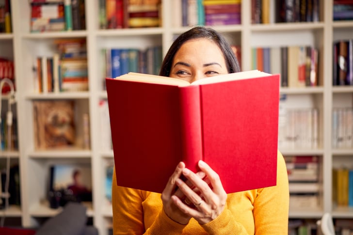 Woman holding book in front of her face and laughing