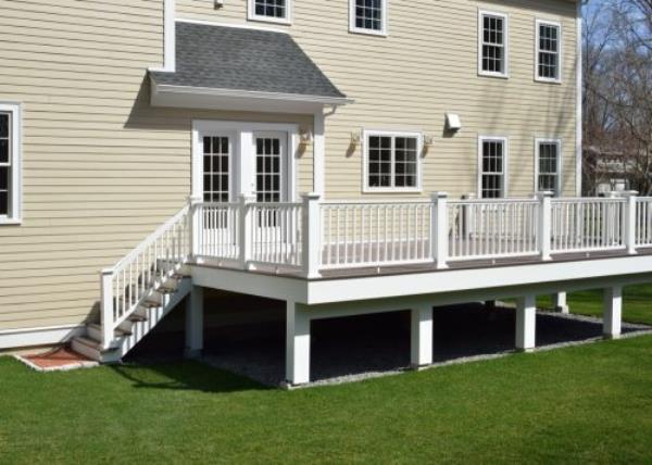 New composite deck. White veranda and railing posts, brown boards, elevated above ground. Showing support f<em></em>rame and gravel under porch.