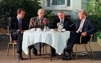The four men sit at a table outdoors, drinking coffee