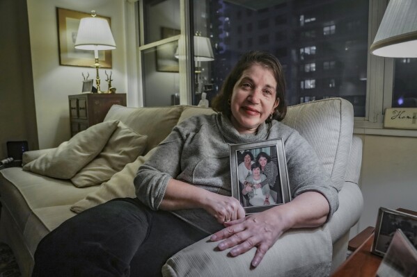 Anne D'Innocenzio shows a portrait of herself, right, with her sister, Do<em></em>nna Burke, left, and mother, Marie D'Innocenzio, as she sits on a sofa from her childhood home, Monday, Feb. 26, 2024, in New York. (AP Photo/Bebeto Matthews)