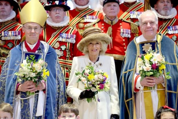 A person holding a bouquet of flowers stands betwee two people in religious vestments also holding bouquets of flowers and in front of retired service members in ceremo<em></em>nial dress.