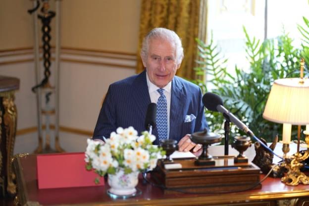 A person sits at a desk behind a microphone and a bouquet of flowers.