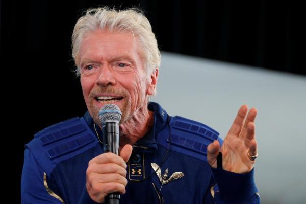 Richard Branson wearing astronaut's wings, holding a microphone at a news conference, after journey to the edge of space with Virgin Galactic in 2021