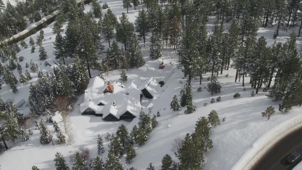 An overview shot of a snowy house and woods. 