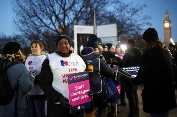 Nurses hold signs outside St. Thomas' Hospital with Big Ben in the background.