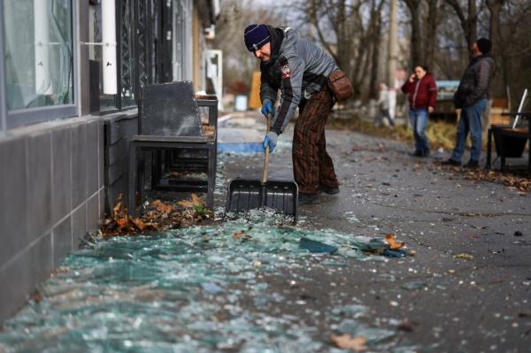 A person cleans up broken glass from a window damaged after a shelling, amid Russia's attack on Ukraine, in Kherson.
