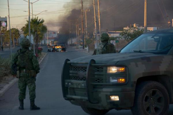 Mexicans soldiers stand guard near burning vehicles.
