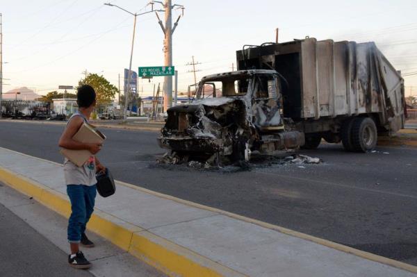 A man passes by a burnt truck on a street during an operation to arrest Guzman.