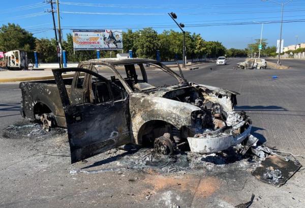 A car was burned after clashes between federal forces and armed groups following Guzman's capture.