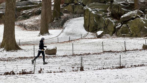 A women running on a trail partially covered with snow powder early Wednesday in Central Park.