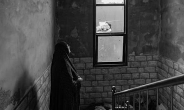 Woman looks out a broken window